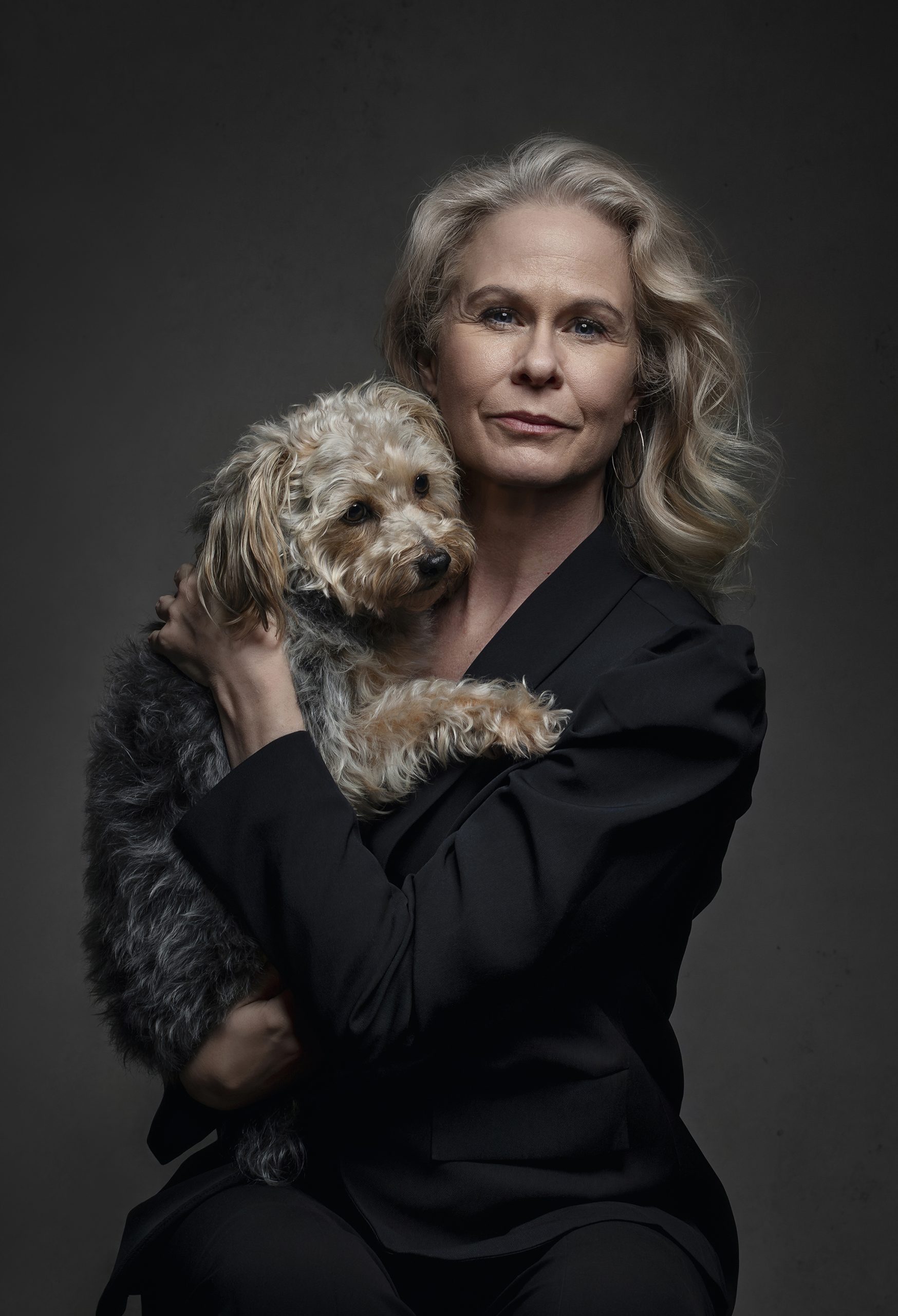 This portrait is of a Blonde-haired woman wearing a black pant suit holding her Yorkie dog.  Part of the Devoted Campaign